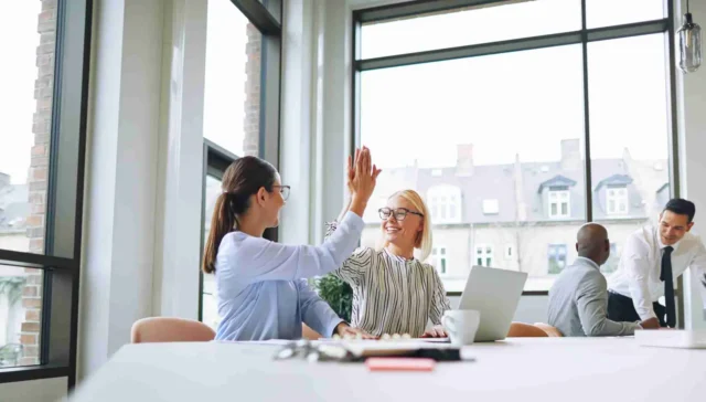 Two smiling businesswomen celebrating with high fives in an office