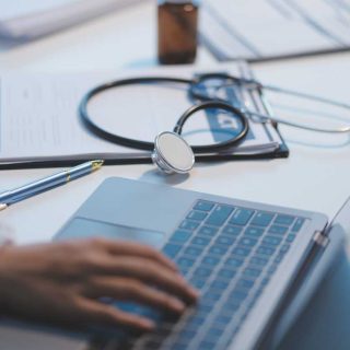 A professional and focused Asian female doctor in scrubs is working and reading medical research on her laptop in her office at a hospital.