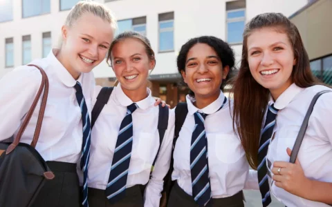 Portrait Of Smiling Female High School Students Wearing Uniform Outside College Building