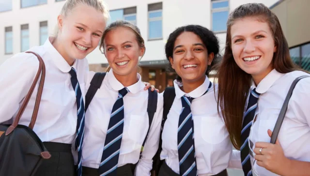 Portrait Of Smiling Female High School Students Wearing Uniform Outside College Building