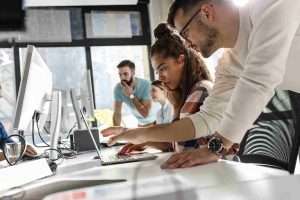 collague point to on laptop, another is watching
