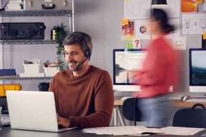 a men working on laptop & a women walking behind him