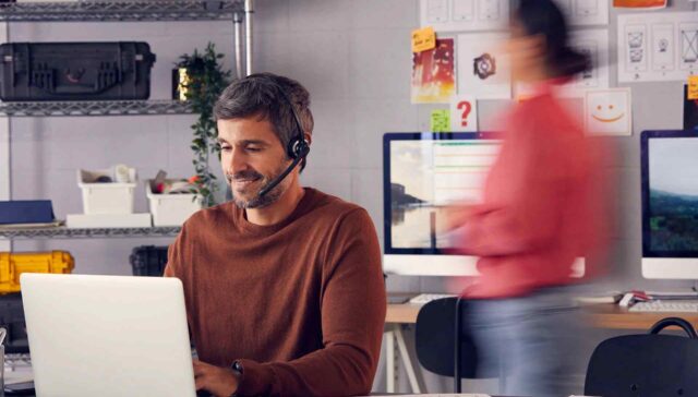 a men working on laptop & a women walking behind him