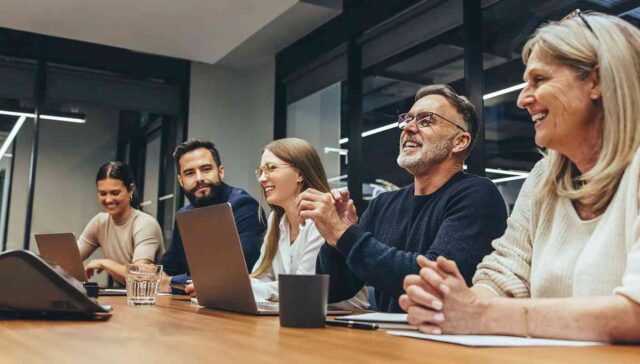 employees laughing on a meeting table during a meeting discussion