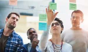Woman leader, team and sticky notes on glass for timeline, strategy and brainstorming in workshop. Female speaker, presentation and group training in boardroom for idea, collaboration and information.