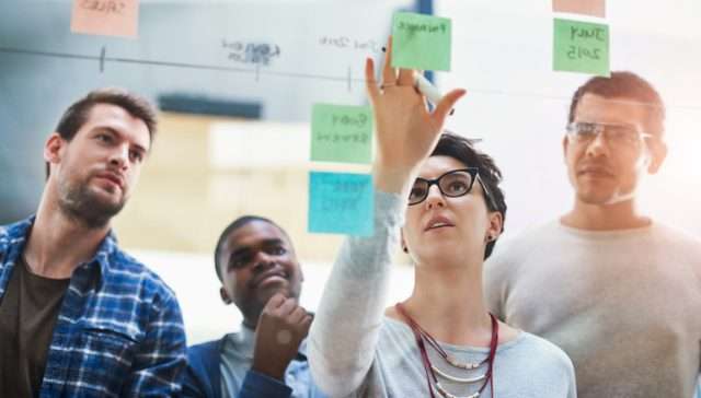 Woman leader, team and sticky notes on glass for timeline, strategy and brainstorming in workshop. Female speaker, presentation and group training in boardroom for idea, collaboration and information.