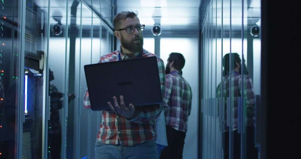 Bearded IT engineer using laptop in server room