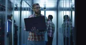 Bearded IT engineer using laptop in server room