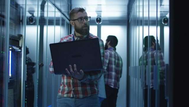 Bearded IT engineer using laptop in server room